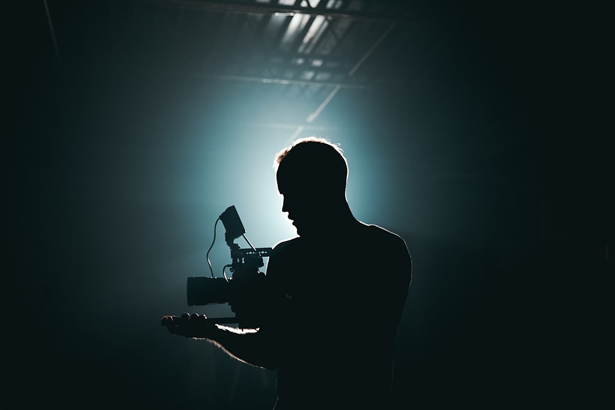 Silhouette d'un cadreur tenant une caméra de cinéma à contre-jour sur un plateau, symbole des productions audiovisuelles et de leur localisation