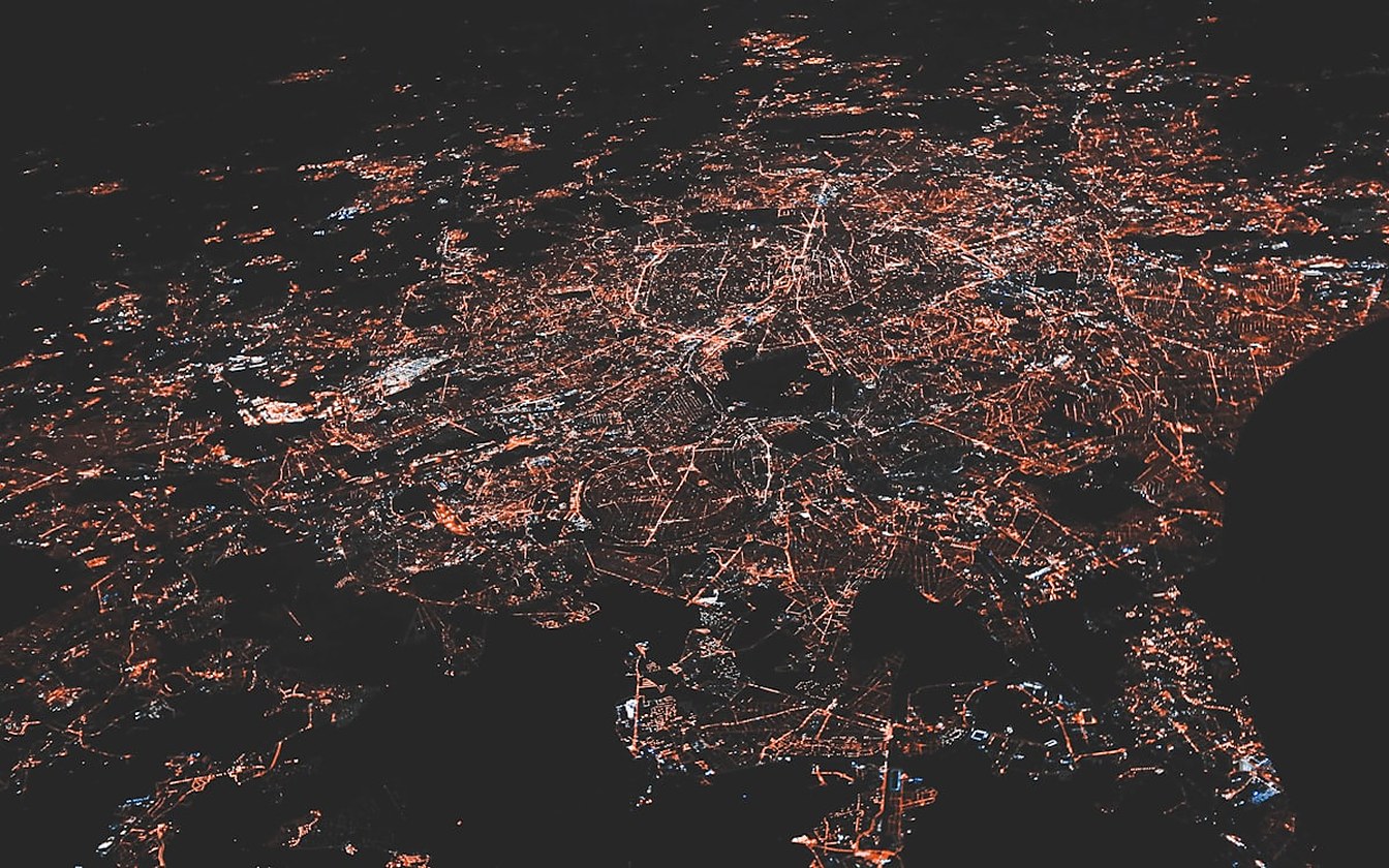 Vista aérea noturna de uma área urbana extensa, com as luzes das ruas e das habitações a desenhar a rede de distribuição elétrica vista do ar