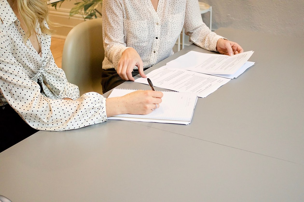 Due persone in abbigliamento professionale che consultano e firmano documenti insieme su un tavolo