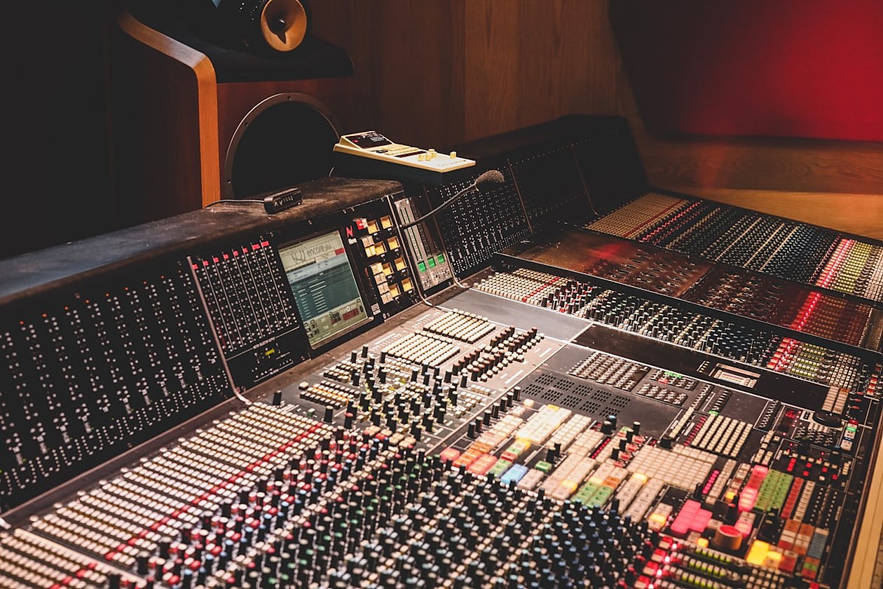 Console di missaggio audio in uno studio di registrazione, con cursori, indicatori luminosi e uno schermo di editing visibili in primo piano