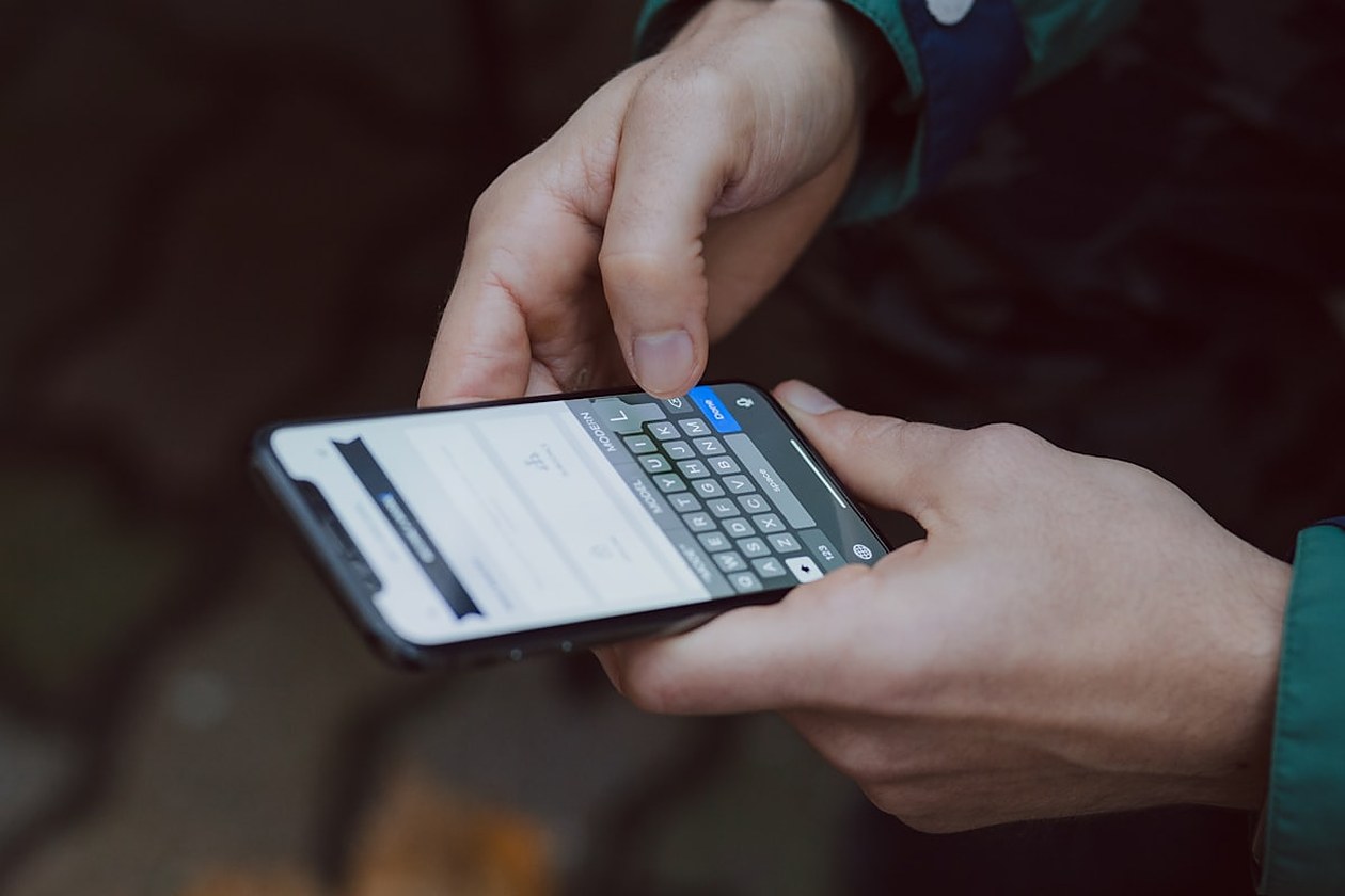 Primer pla d'unes mans sostenint un telèfon mòbil i teclejant-hi, amb un jaqueta verd fosc de fons